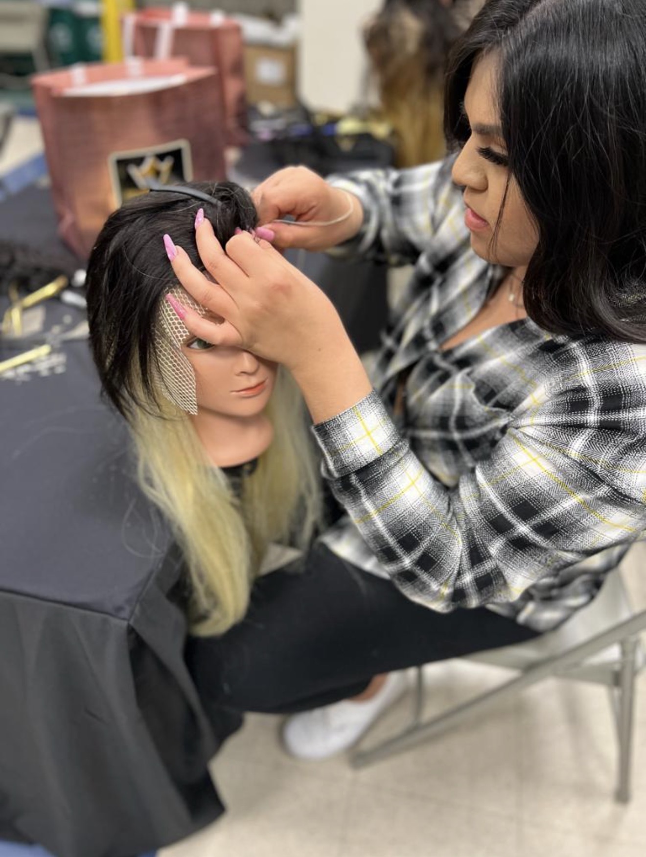 A practitioner fitting and sewing a hairpiece base onto a mannequin head during an iHobbs Academy training session.