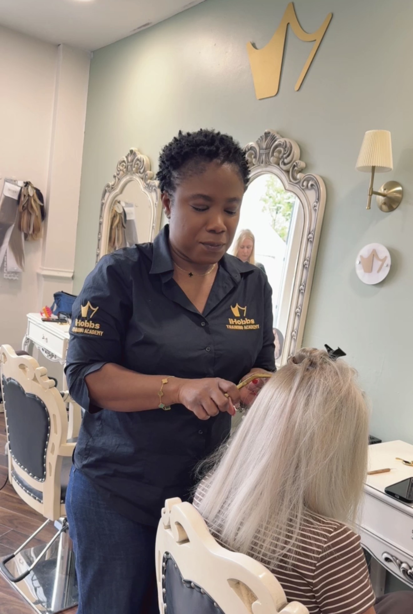 Sandra Atoge, wearing an iHobbs Training Academy top, working on a client's hair in the salon.