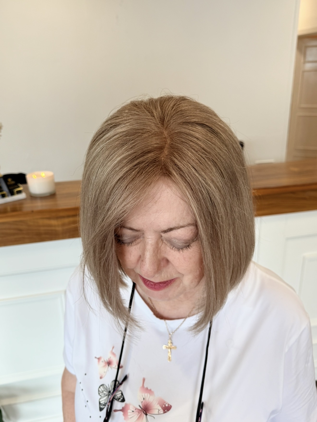 A woman looking down, showing the parting and natural fall of a straight, light-brown bob from a finished Custom Wig.